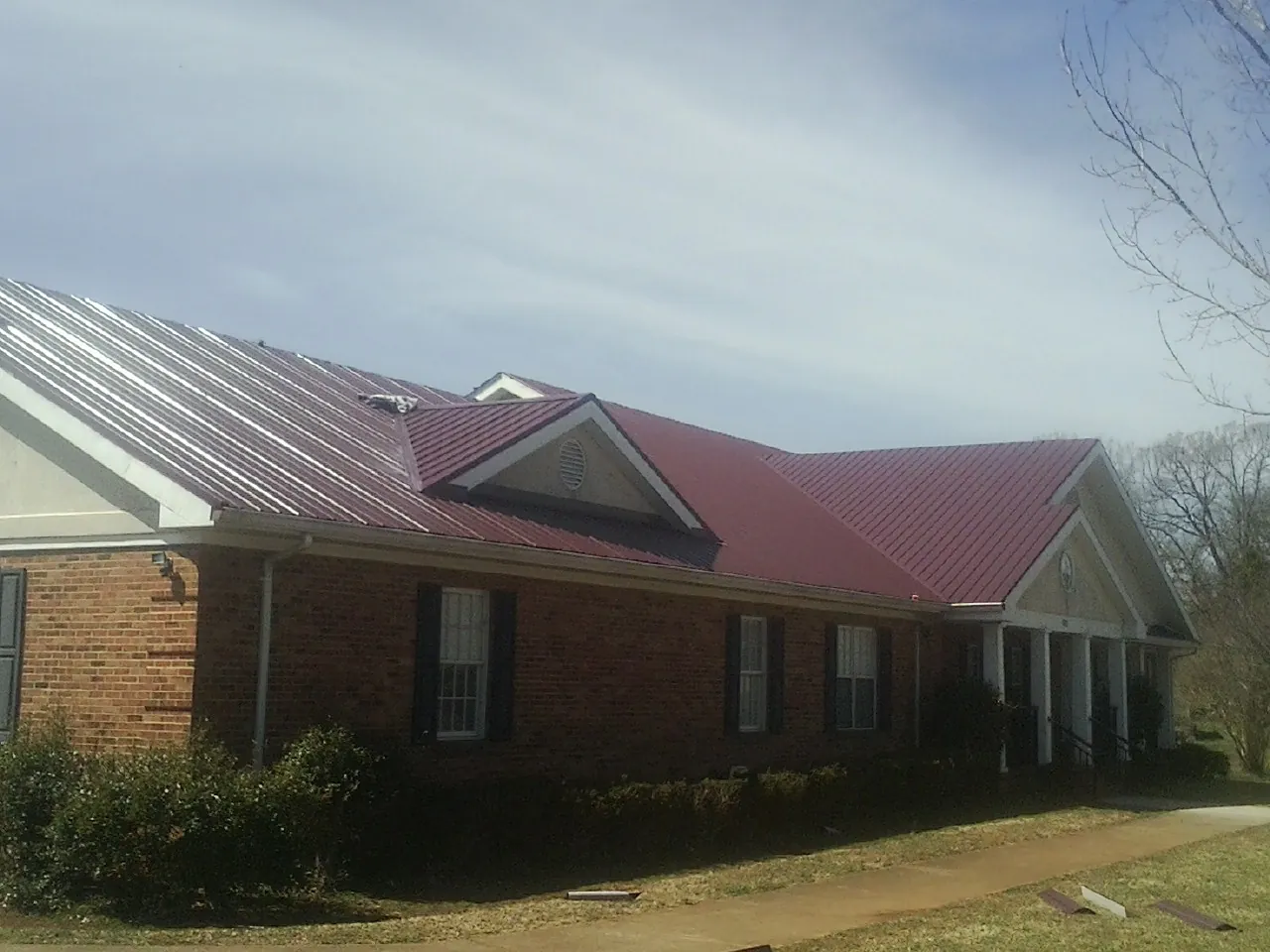 Red metal roof with gabled entries on a long brick building, from a Hail Damage Roof Repair job in Southbury