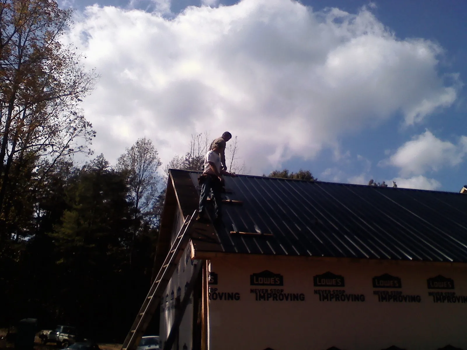 Roofer fastening dark metal panels high against a cloudy sky, from a Roof Inspection job in Southbury