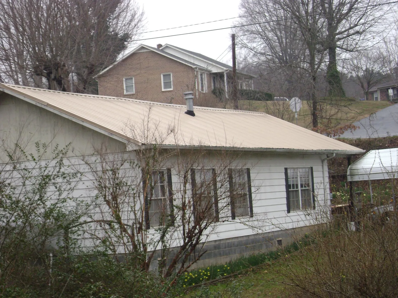 Tan metal roof on a white sided house set into a hillside — Commercial Roofing by Roofing Brothers in Southbury